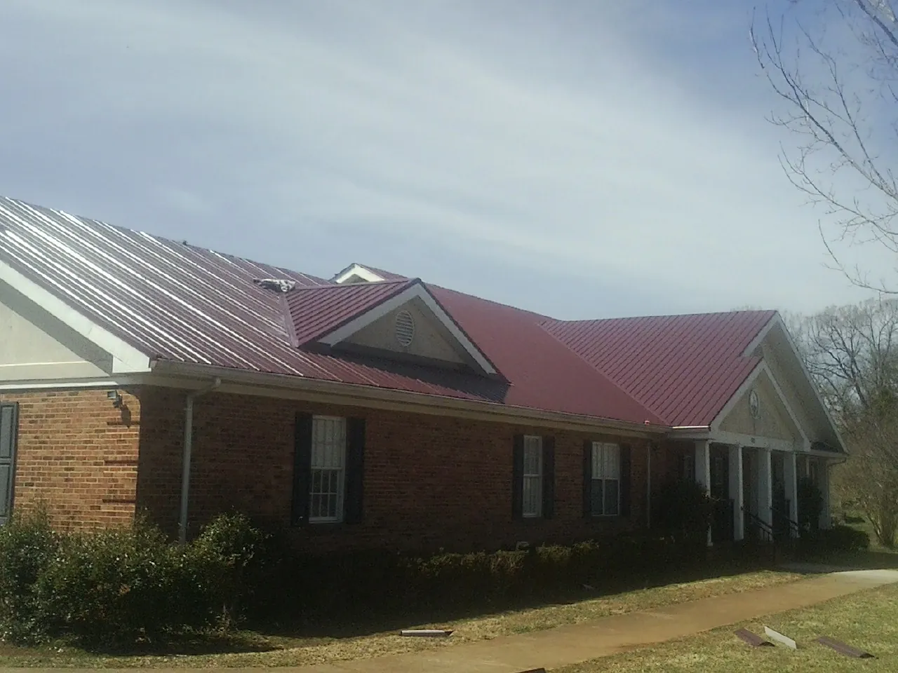 Red metal roof with gabled entries on a long brick building, from a Hail Damage Roof Repair job in Argyle