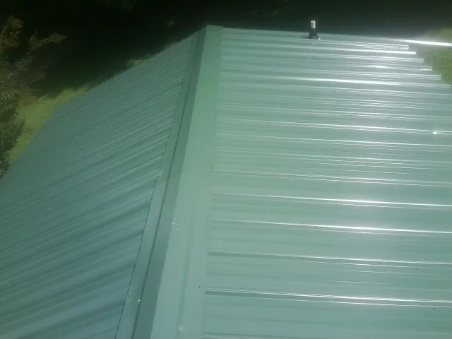 New green metal panels meeting at the ridge of a roof — Flat Roof Repair work by our crew in Argyle