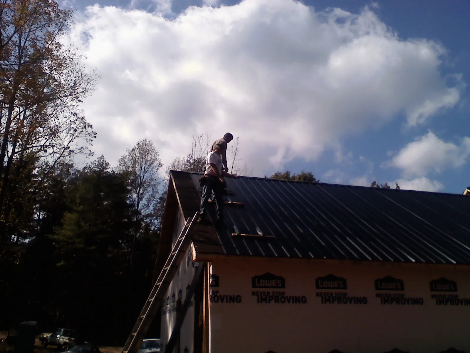 Roofer fastening dark metal panels high against a cloudy sky, from a Roof Inspection job in Argyle